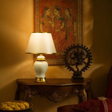 White ceramic table lamp with golden base and tapered fabric shade adding warm lighting to traditional decor.