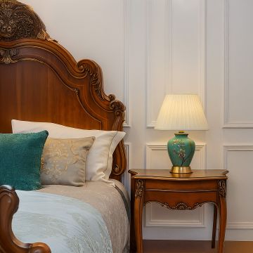 Green ceramic table lamp with floral hand-painted design and pleated fabric shade adding elegance to bedroom decor.