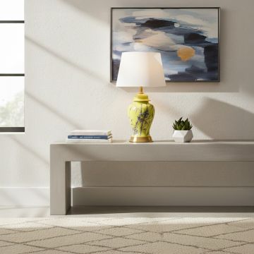 Yellow ceramic table lamp with hand painted bamboo bird artwork gold metal base and fabric shade styled on side table.