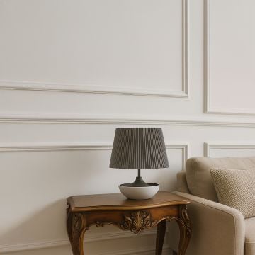 Grey pleated table lamp with a black and white ceramic base placed beside an upholstered sofa creating a clean modern accent in a neutral living space.