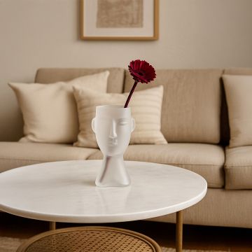 Frosted glass vase in abstract face design white finish styled with red flower on round coffee table in modern living room decor.