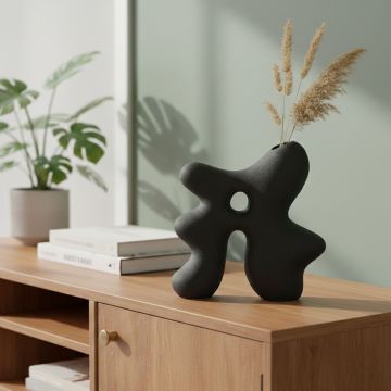 Dark grey ceramic abstract hollow vase styled on console table for modern living room decor accent.