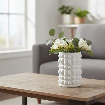 White ceramic textured vase with fresh flowers placed on wooden table adding modern elegance to living room decor.