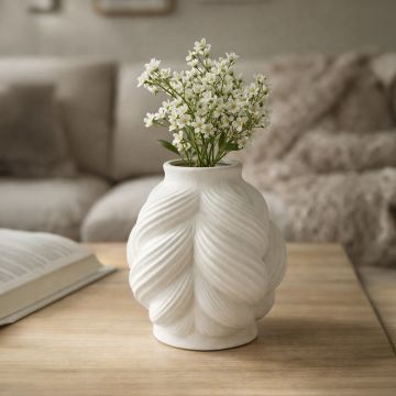 White ceramic sculpted vase with fresh flowers placed on wooden table adding soft elegance to cozy living room decor.
