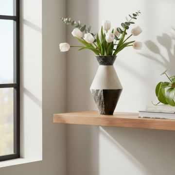 White and black ceramic decorative vase with floral stems placed on wooden shelf adding modern elegance to living room decor.