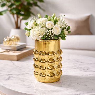 Gold metal textured decorative vase with white flowers placed on marble table adding luxurious and elegant touch to living room decor.