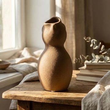 Brown ceramic sculpted vase placed on wooden side table adding warm earthy charm to cozy living room decor.
