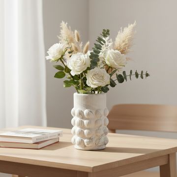 White ceramic textured vase with floral arrangement styled on wooden table enhancing elegant and cozy living room decor.