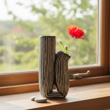 Black and white striped ceramic vase with red flower styled on window sill enhancing contemporary home decor.