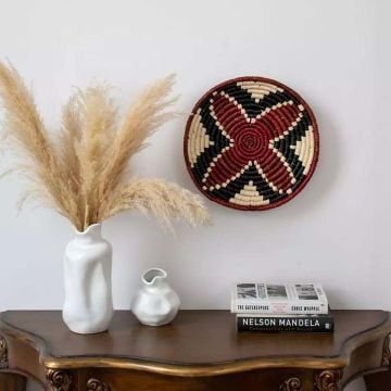 Beautiful red black and natural woven wall plate styled on a wooden console table with pampas grass and ceramic vases for elegant home décor.