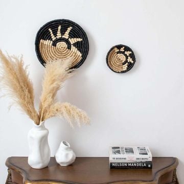 Black and beige bamboo wall plates styled above wooden table with pampas vase adding natural charm to modern decor.