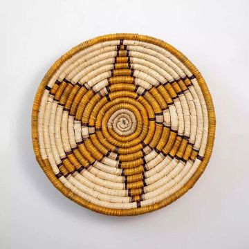 Round woven basket wall decor on white background with starburst design in beige and brown handmade natural materials.