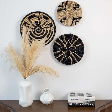 Handcrafted woven baskets in black and beige displayed on a white wall with decorative pampas grass in a modern living space.