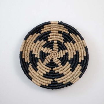 Handwoven wicker wall decor plate in beige and black round natural fiber spiral design light on white background for styling.