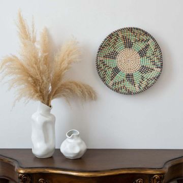 Handwoven wicker wall plate decor in beige green and navy design styled on wall with boho home decor setup.