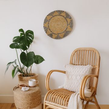 Handwoven wicker wall plate decor in yellow navy and beige design styled on wall with rattan chair and boho home setup.