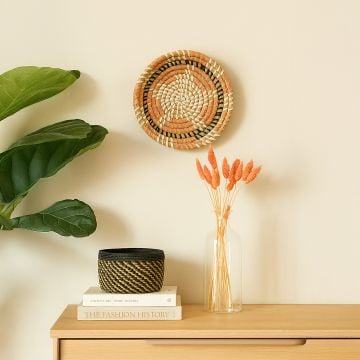Handwoven wicker basket wall decor styled with books vase and greenery for modern boho home interior decoration.