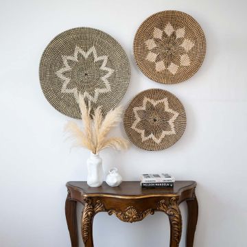 Handwoven wicker basket wall decor styled with pampas grass vase and books on wooden console for boho home interiors.