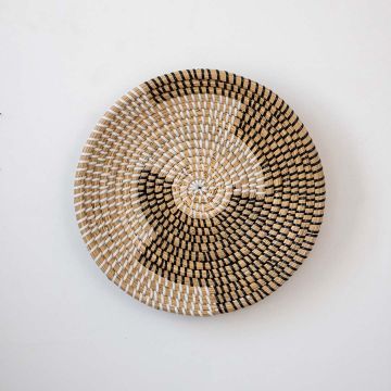 Handwoven wicker basket wall decor in beige with black and white swirl woven pattern on clean white background.