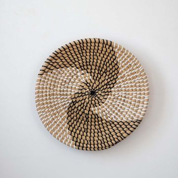 Handwoven wicker basket wall decor in beige with black and white spiral woven pattern design on clean white background.