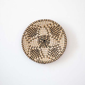 Handwoven wall basket decor in natural and black tones with boho design on white background.