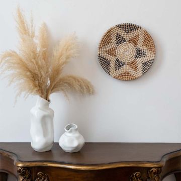 Handwoven wall basket decor styled with vases on wooden console table for rustic boho living room wall.