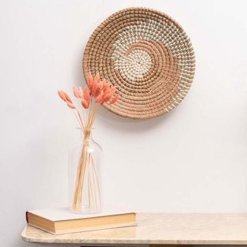 Handwoven wall basket decor in natural and pink fiber styled with vase and books for boho wall decoration.