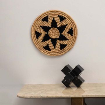 Natural seagrass wall plate with black star design arranged on a plain wall above a wooden table for minimalist bohemian styling.