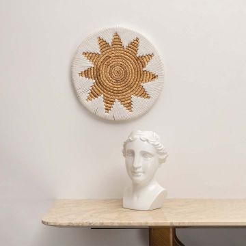 A handcrafted beige and white jute wall plate with sunburst pattern hanging above a cozy seating space adding soft earthy decor to a modern minimal living room.