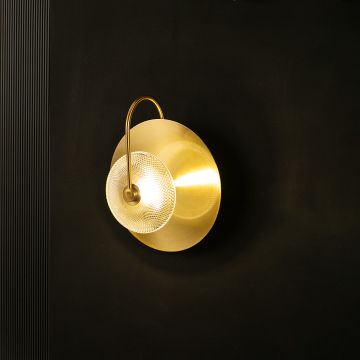 Contemporary brass wall light with clear glass detail illuminated warmly on dark background.