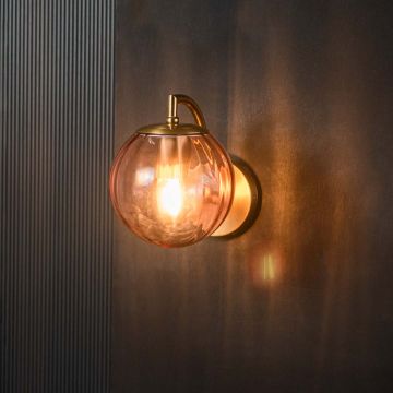Decorative pink glass wall light with brass fixture glowing warmly against black background interior.