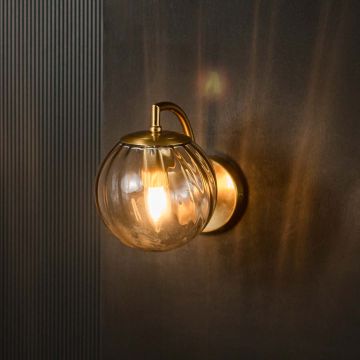 Modern grey glass wall light with brass fixture glowing warmly against black background interior.