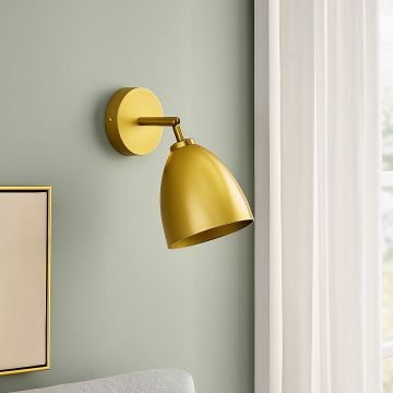 Modern gold wall sconce with metallic dome shade mounted beside curtains on soft green wall.