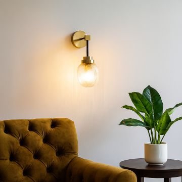 Elegant gold and black wall sconce with textured glass shade glowing warmly beside sofa and indoor plant for modern home décor.
