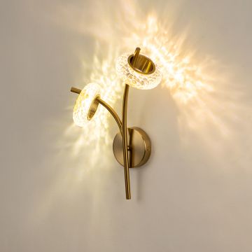 A gold wall sconce with two curved arms and textured glass ring shades shown with lights on against a white background highlighting its warm radiant glow.