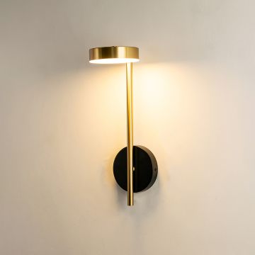 A slim vertical metal wall light with a circular head casting soft downward illumination on a beige backdrop adding minimal warm lighting and refined modern décor.