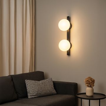Wall-mounted light with dual frosted glass shades and black body enhances cozy corner with sofa and decor.