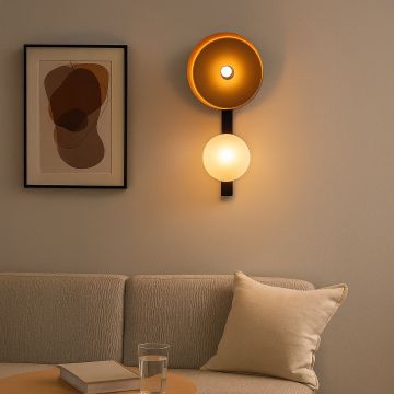Decorative wall lamp with gold bowl shade and frosted globe mounted above beige sofa in cozy living room.