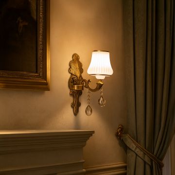 Elegant one light crystal sconce with gold base and white shade glowing warmly in classic living room decor.
