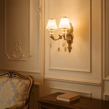 Elegant two light crystal sconce with gold base and white shades glowing warmly in classic living room decor.
