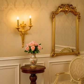 Golden wall light with dual candle style design illuminating elegant living room decor with mirror and flowers.