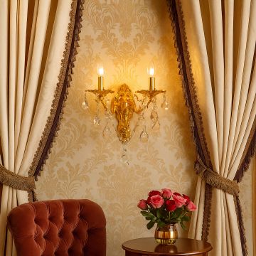Golden wall light with crystal drops glowing elegantly between curtains above table with roses in luxury interior.