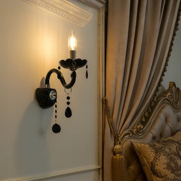 Black wall light with crystal drops glowing beside luxury bed with golden headboard and curtains in bedroom.