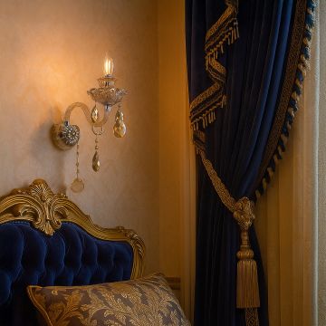 Elegant crystal wall light glowing in luxury bedroom with golden headboard and royal blue curtains decor.