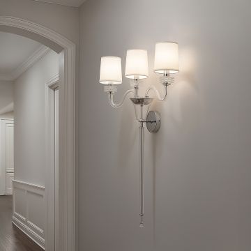 Triple arm wall light with chrome base and fabric shades glowing in modern hallway with neutral wall decor.