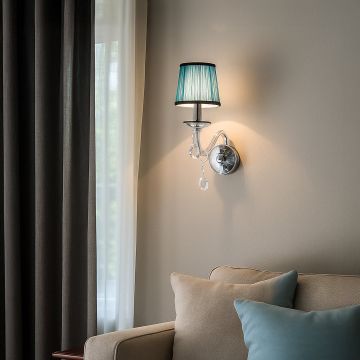 Modern wall light with chrome base blue fabric shade and crystal drops glowing beside sofa and curtains.