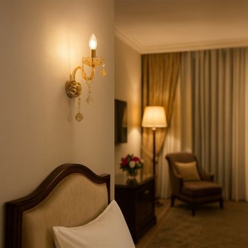 Golden wall light with crystal drops glowing above bed in elegant bedroom interior with lamp chair and curtains.