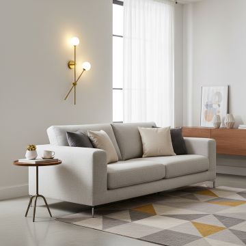 A modern double globe brass wall light glowing warmly on a deep blue wall beside a beige sofa and a wooden console creating a calm contemporary setting.