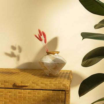 Lifestyle view of a handcrafted ceramic vase styled on a woven wicker chest with soft light pink dried florals creating a calm modern Decor setting.