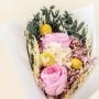 Closeup of preserved flower bouquet with pink roses yellow billy button white hydrangea and maroon crystal grass creating a decorative floral gift.